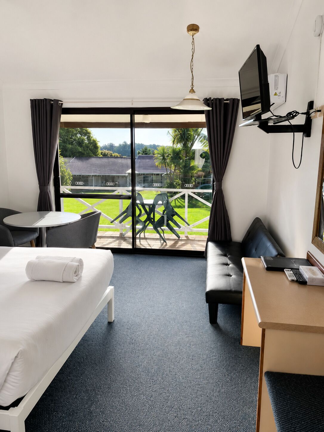 Een hotelkamer met een bed, een bureau, een stoel, een bank en een balkon met uitzicht op de omgeving.