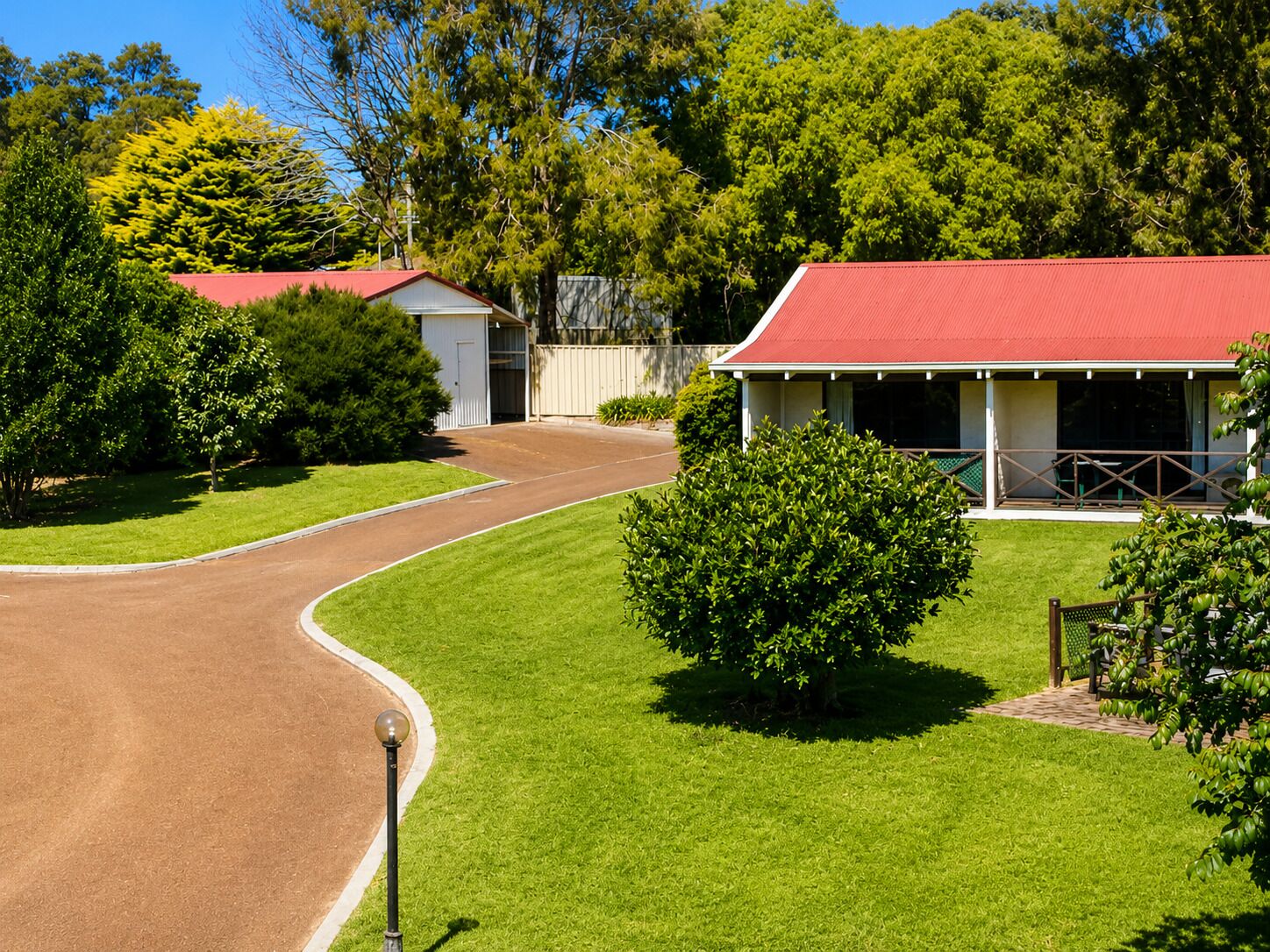 A residential area with a paved driveway, a small building with a red roof, and surrounding greenery.