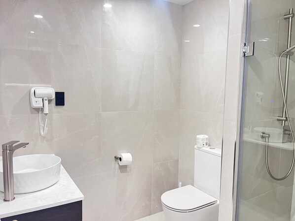 A modern bathroom with a glass-enclosed shower, a white toilet, and a sink with a faucet.