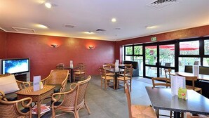A restaurant with wicker furniture, a TV, and large windows. - Manukau Hotel & Conference Centre (Auckland)