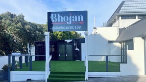 A sign for 'Bhojan Indian Restaurant & Bar' with a clear entrance and a well-maintained lawn. - Manukau Hotel & Conference Centre (Auckland)
