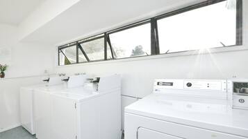 A laundry room with two white washers and dryers, a window above the dryers, and a small potted plant on the left.