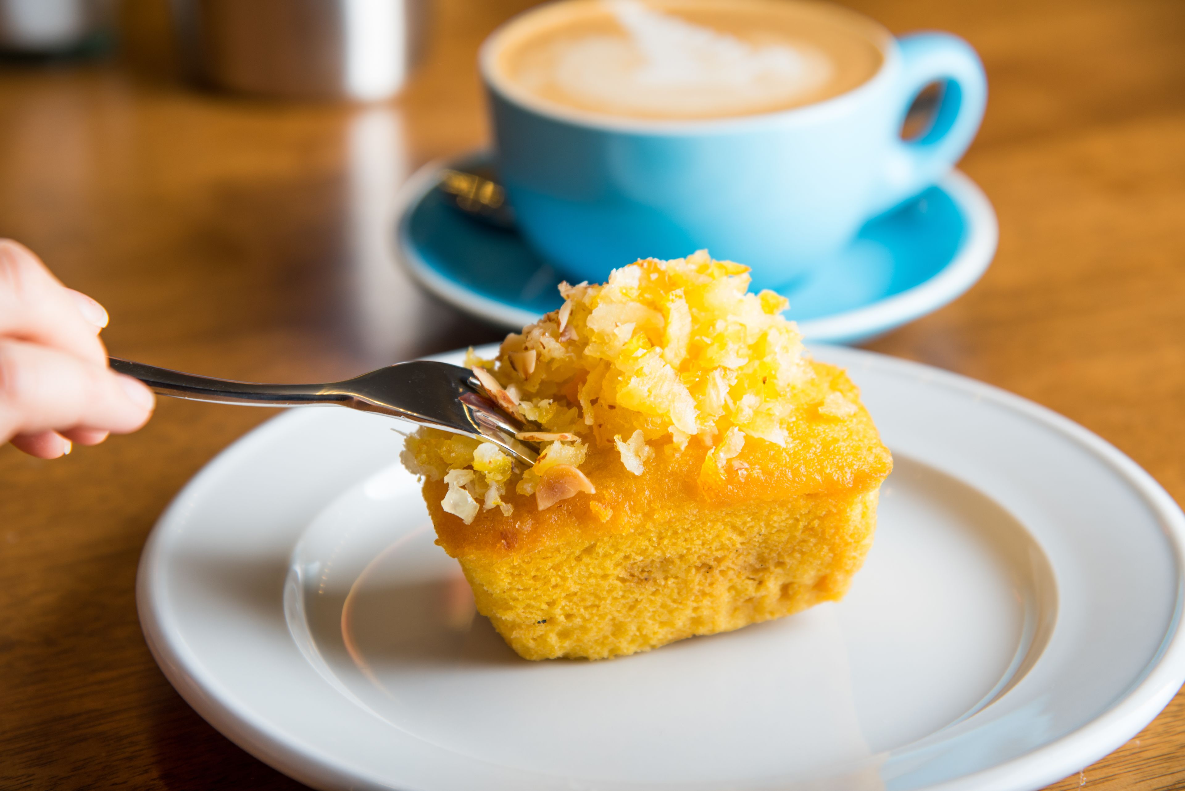 A slice of cake on a white plate with a blue cup of coffee in the background.