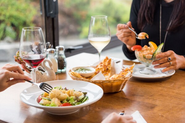 A dining table with a variety of dishes, including a salad, shrimp, and bread, along with glasses of wine.