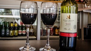 Dos copas de vino tinto con una botella de vino Villa Maria sobre una barra.