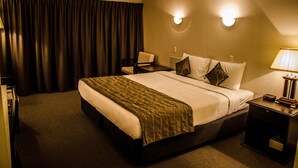 Una habitación de hotel con una cama grande, una mesita de noche, una silla y una lámpara.