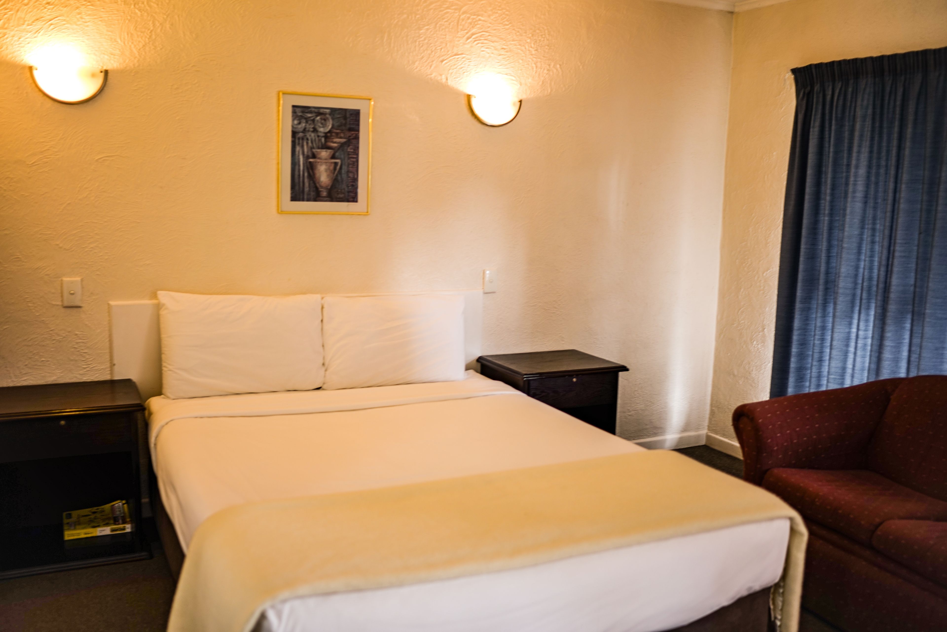 Une chambre d’hôtel comprenant un lit, deux tables de chevet, une petite table, une chaise et un tableau accroché au mur.