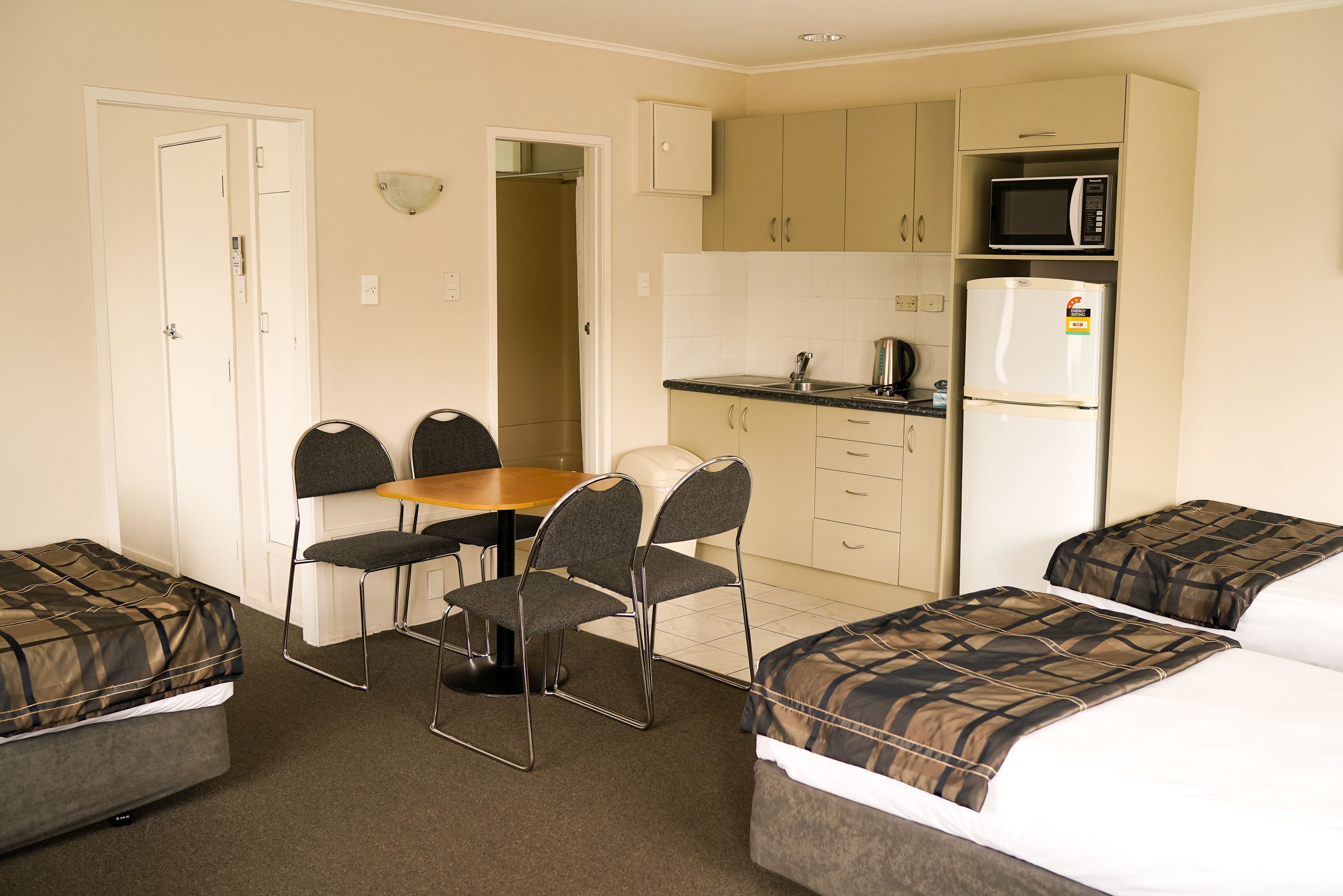 A compact hotel room with a kitchenette, a dining area with a table and chairs, and two single beds.