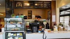 Una barra de café con un menú, una máquina de café y una vitrina con pasteles.