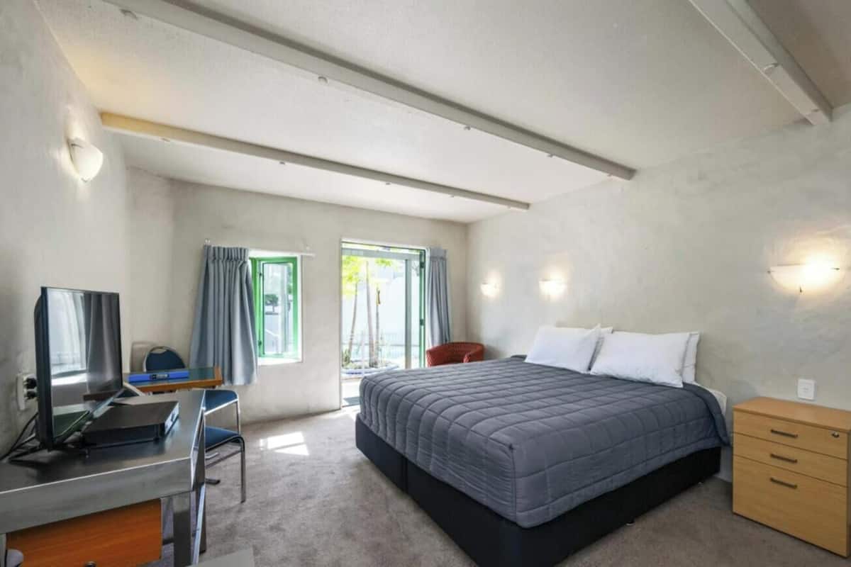 Un dormitorio con cama, escritorio, silla y un pequeño armario de madera.