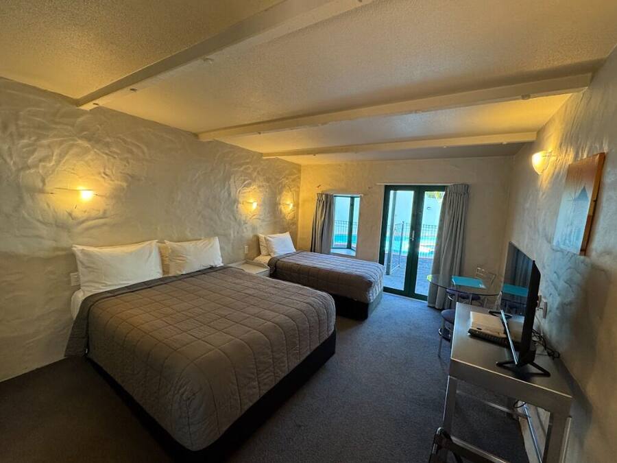 A hotel room with two beds, a desk with a computer, and a view of the outdoors.