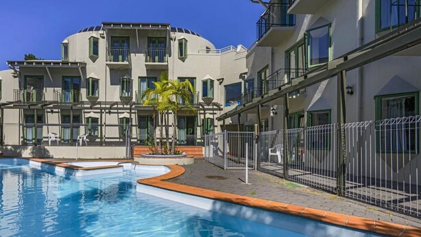 Una piscina de borde curvo, un edificio con balcones y una palmera.