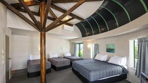 Una habitación con una cama grande, dos camas más pequeñas, una viga de techo de madera y un tragaluz.