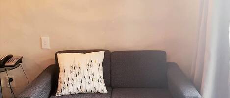 Um sofá cinzento com uma almofada estampada, uma pequena mesa com um teclado e duas luminárias fixadas na parede.