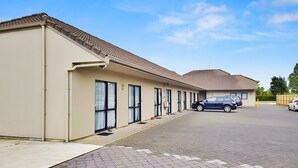 Ein Gebäude mit Ziegeldach, mehreren Eingängen und einem gepflasterten Parkplatz mit Autos.