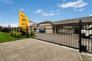 Un área cercada con un letrero amarillo para AKL Airport Motel, un camino pavimentado y un edificio con techo de tejas.