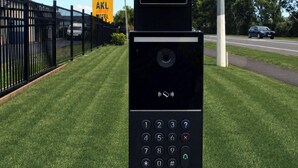 A gate access kiosk with instructions for checking a welcome email for a gate code and pressing a green bell button for assistance. - Auckland Airport Motel (Auckland)