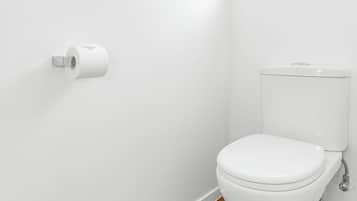 Inodoro blanco con suelo de madera, pared blanca y un cuadro enmarcado encima.