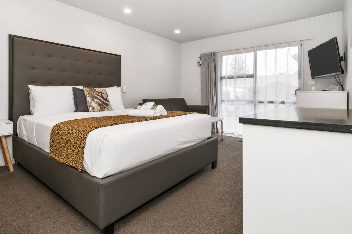 A modern hotel room with a large bed, a flat-screen TV, and a large window.