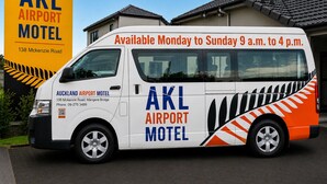 Ein weißer Van mit der Aufschrift 'AKL Airport Motel', geparkt vor einem Gebäude mit dem Schild 'AKL Airport Motel'.