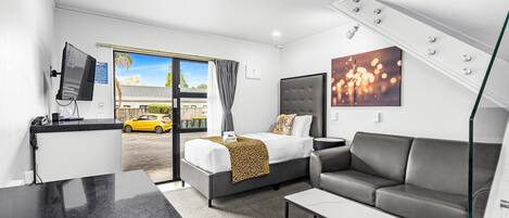 A modern hotel room with a bed, grey sofa, and a desk.