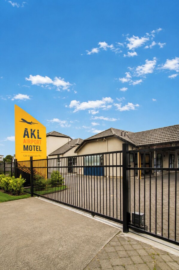 Señal amarilla del Motel AKL Airport con cielo despejado y área de estacionamiento con portón.