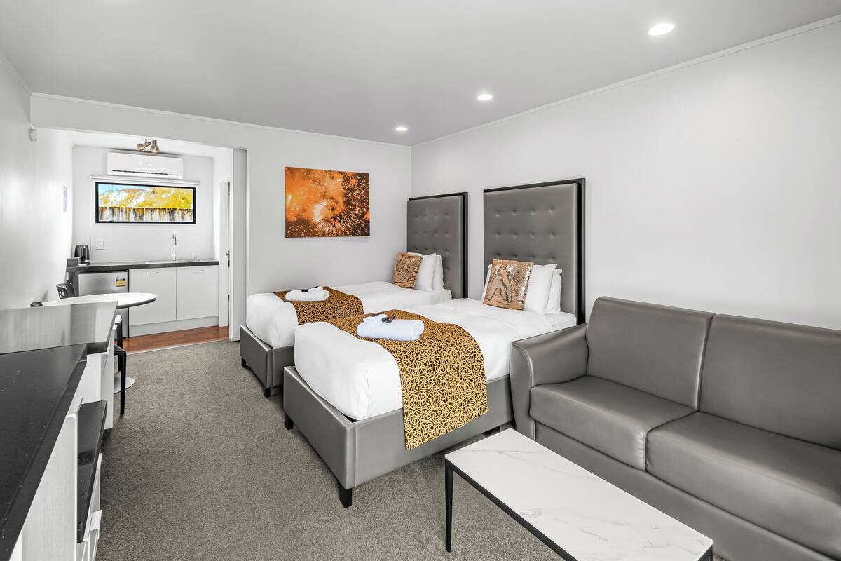 A modern hotel room with two beds, a sofa, a dining area, and a TV.