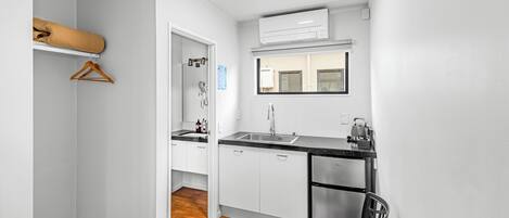 Cocina compacta con armarios blancos, un refrigerador de acero inoxidable y una encimera negra.