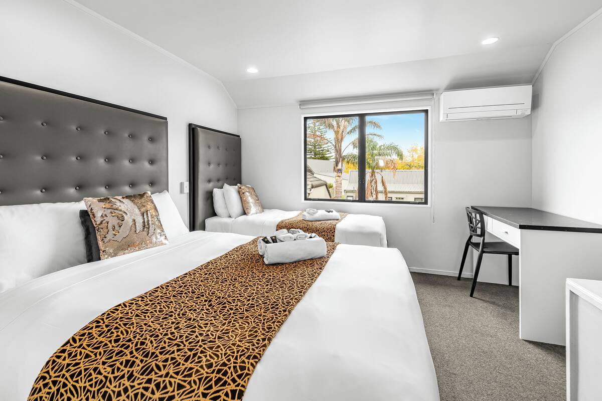 A modern hotel room with a large bed, a desk, and a window with a view of palm trees.
