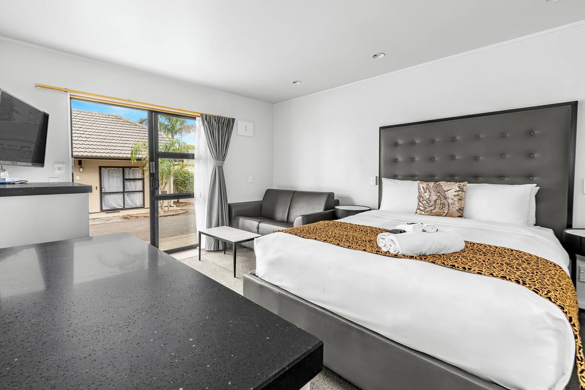 A modern hotel room with a large bed, a desk, a chair, and a TV.