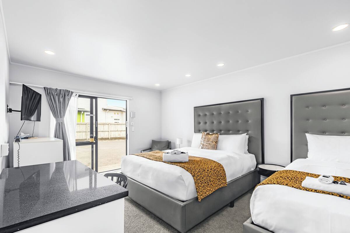 A modern hotel room with two beds, a desk, and a view of the outside.