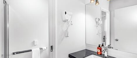 A modern bathroom with a white vanity, a large mirror, a hairdryer, and a towel rack.