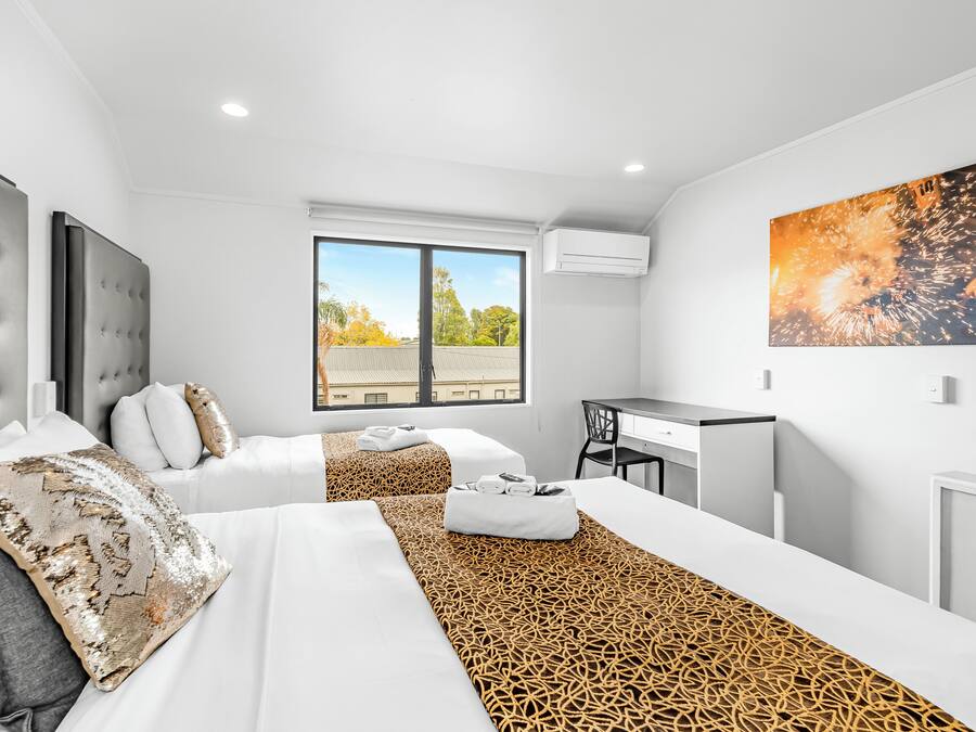 A modern hotel room with two beds, a desk, and a large window offering a city view.