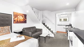 Habitación de hotel moderna con cama, sofá, una mesita, una escalera y una kitchenette.