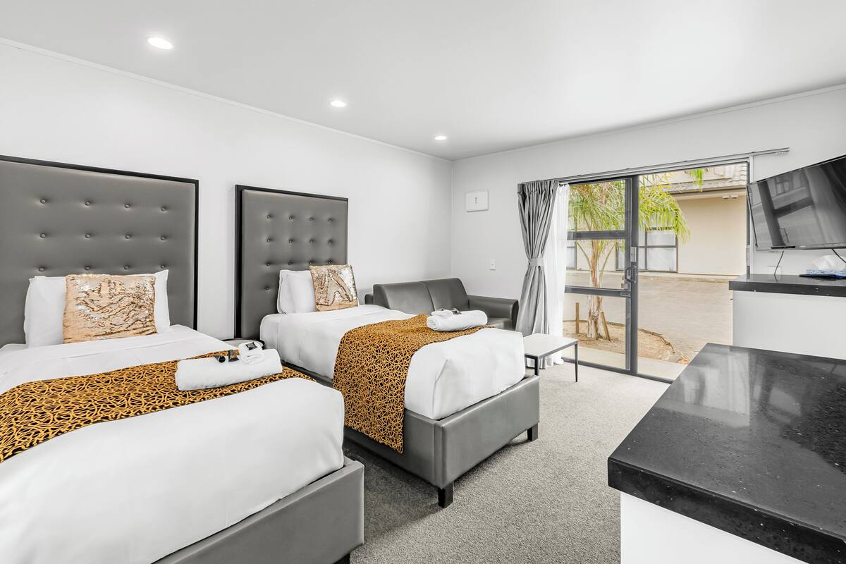 A hotel room with two beds, a TV, and a sliding glass door to the outside.