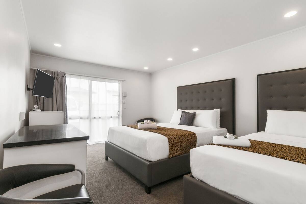 A hotel room with two beds, a desk, a chair, and a TV.