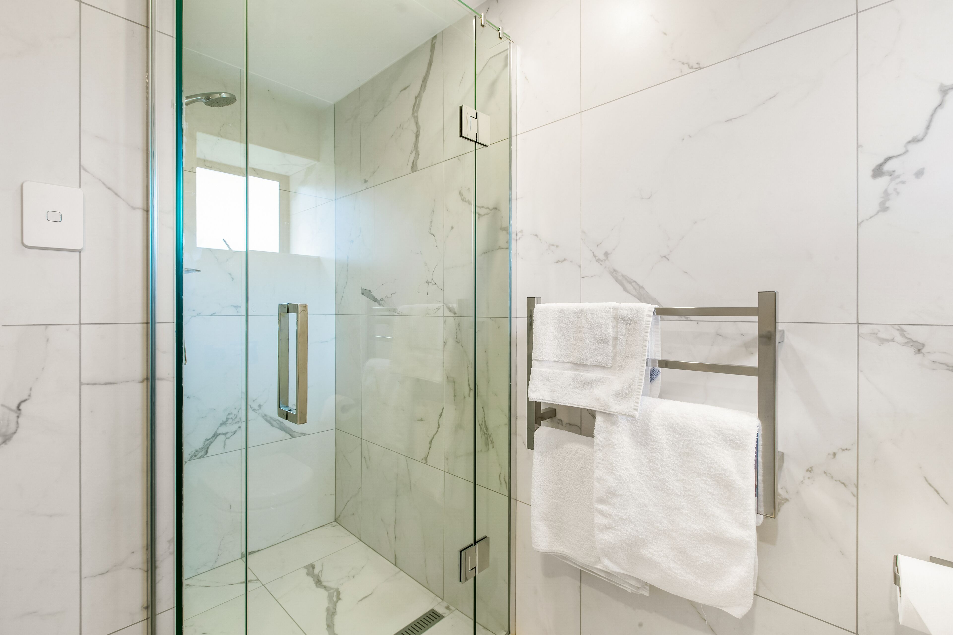 A modern bathroom with a glass-enclosed shower, marble tiles, and a towel rack with multiple towels.