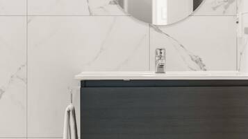 Un baño con pared de azulejos de mármol, un espejo redondo, un tocador de madera oscura y un perchero para toallas.