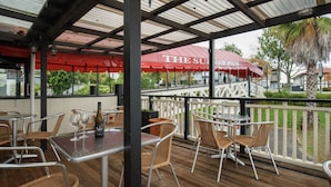 An outdoor patio area with tables and wicker chairs, a red umbrella, and a view of a building with a sign that reads "THE SURF HOUSE". - The Surrey Hotel (Auckland)