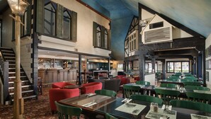 A restaurant with a high ceiling, exposed beams, and a mix of red and green upholstered chairs. - The Surrey Hotel (Auckland)