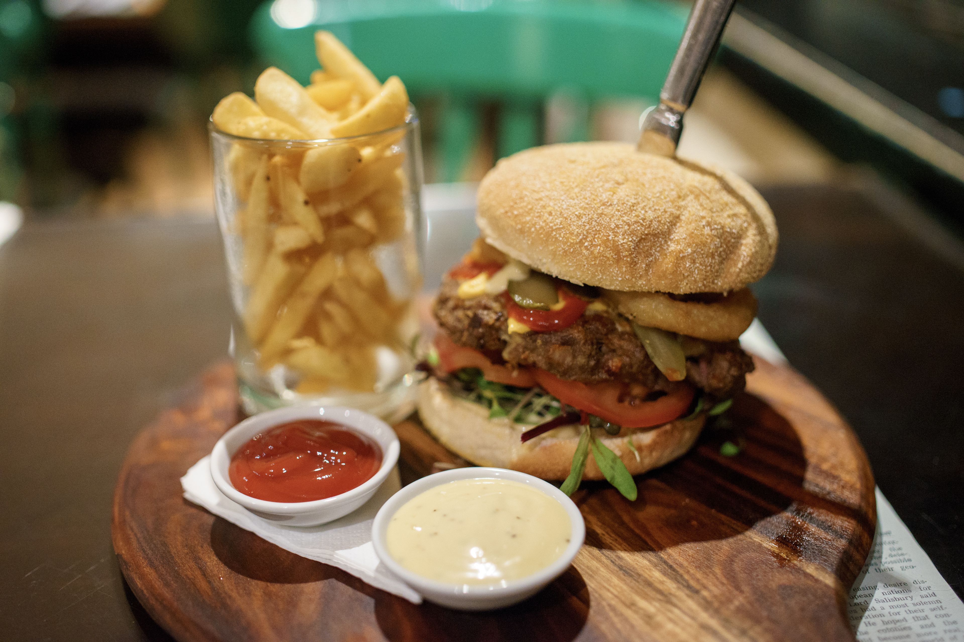 A burger with fries and two dipping sauces on a wooden board.
