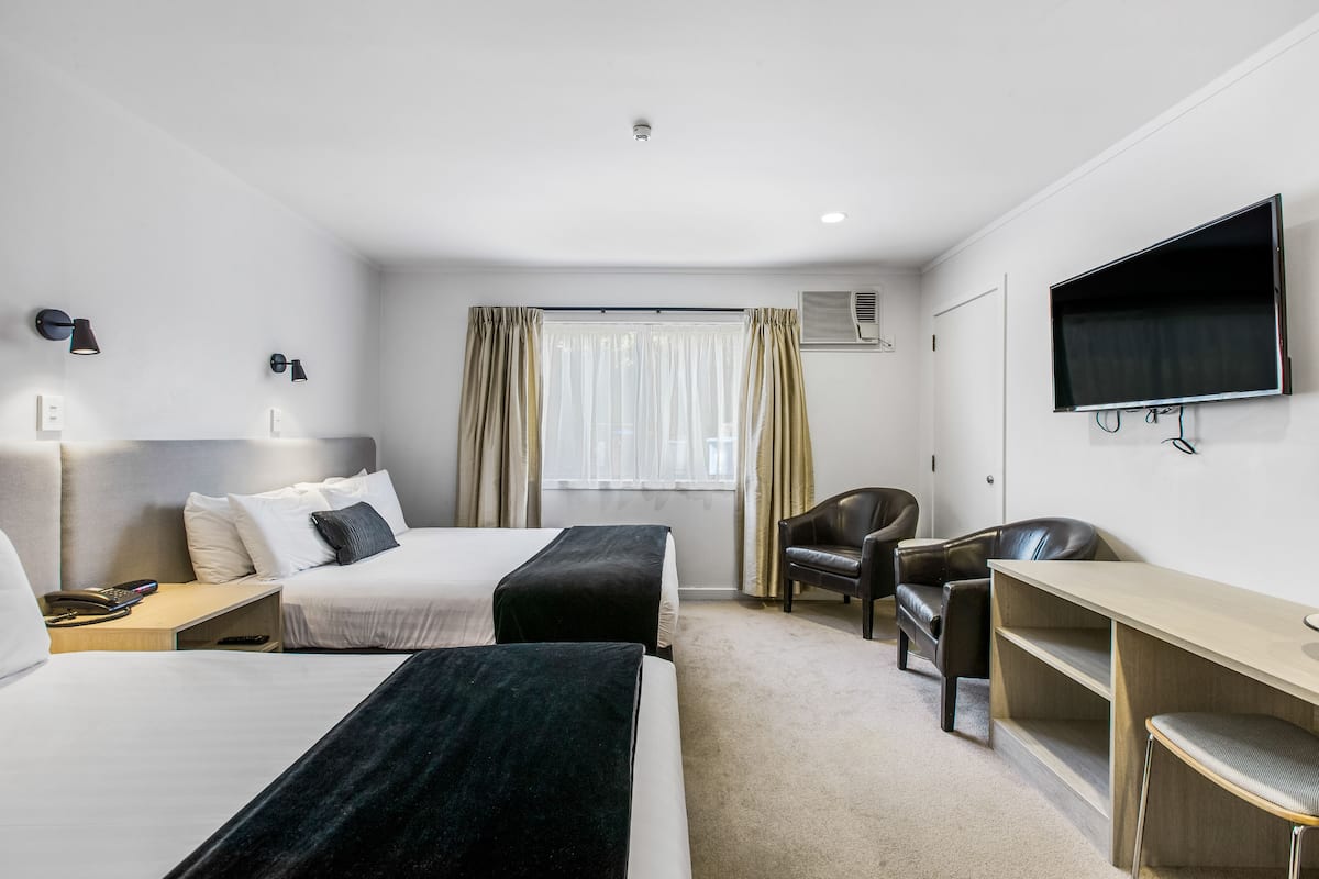 Quarto de hotel com duas camas, uma mesa, uma cadeira, uma televisão e janela com cortinas.