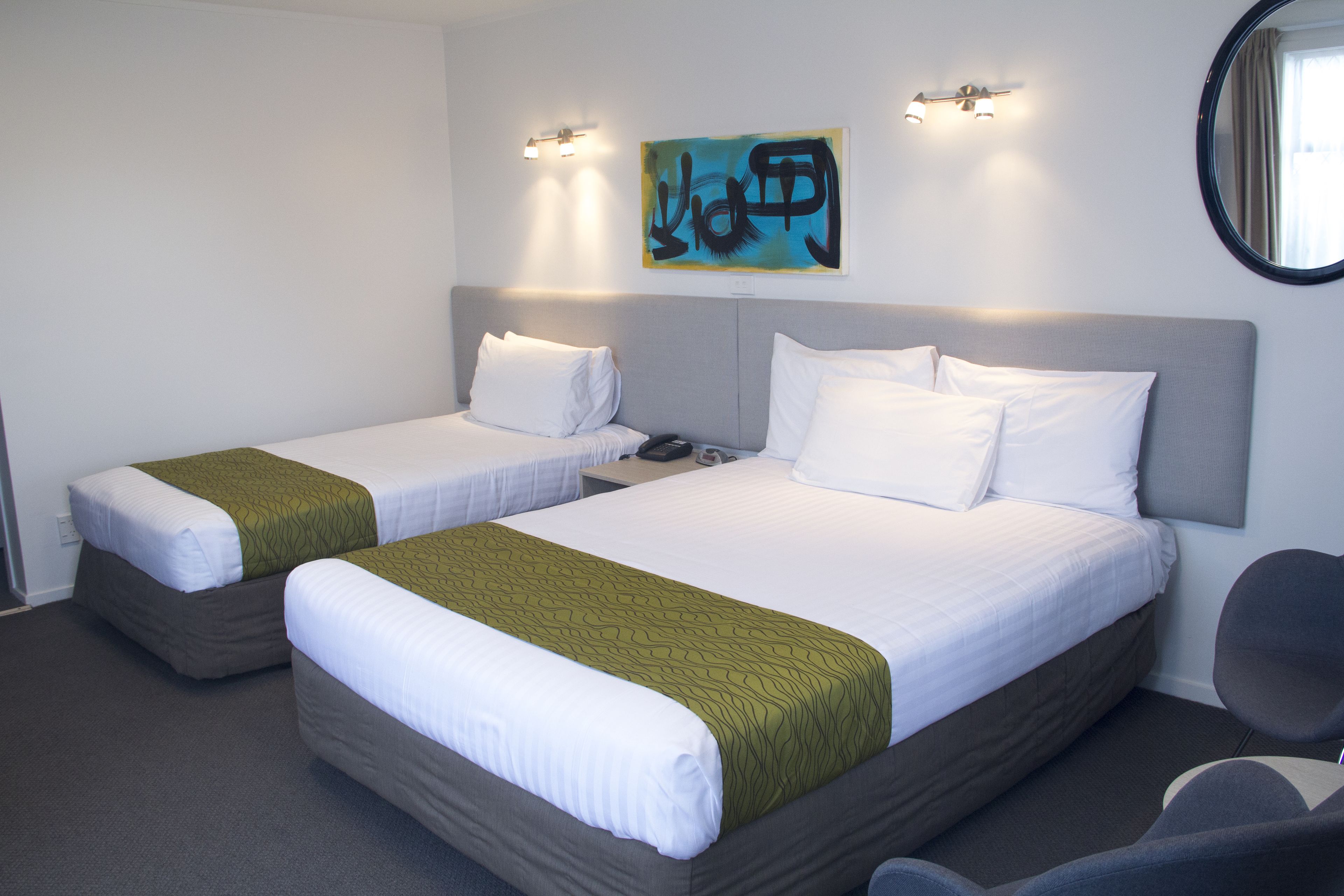 Habitación de hotel con dos camas individuales, un espejo grande y un cuadro en la pared.