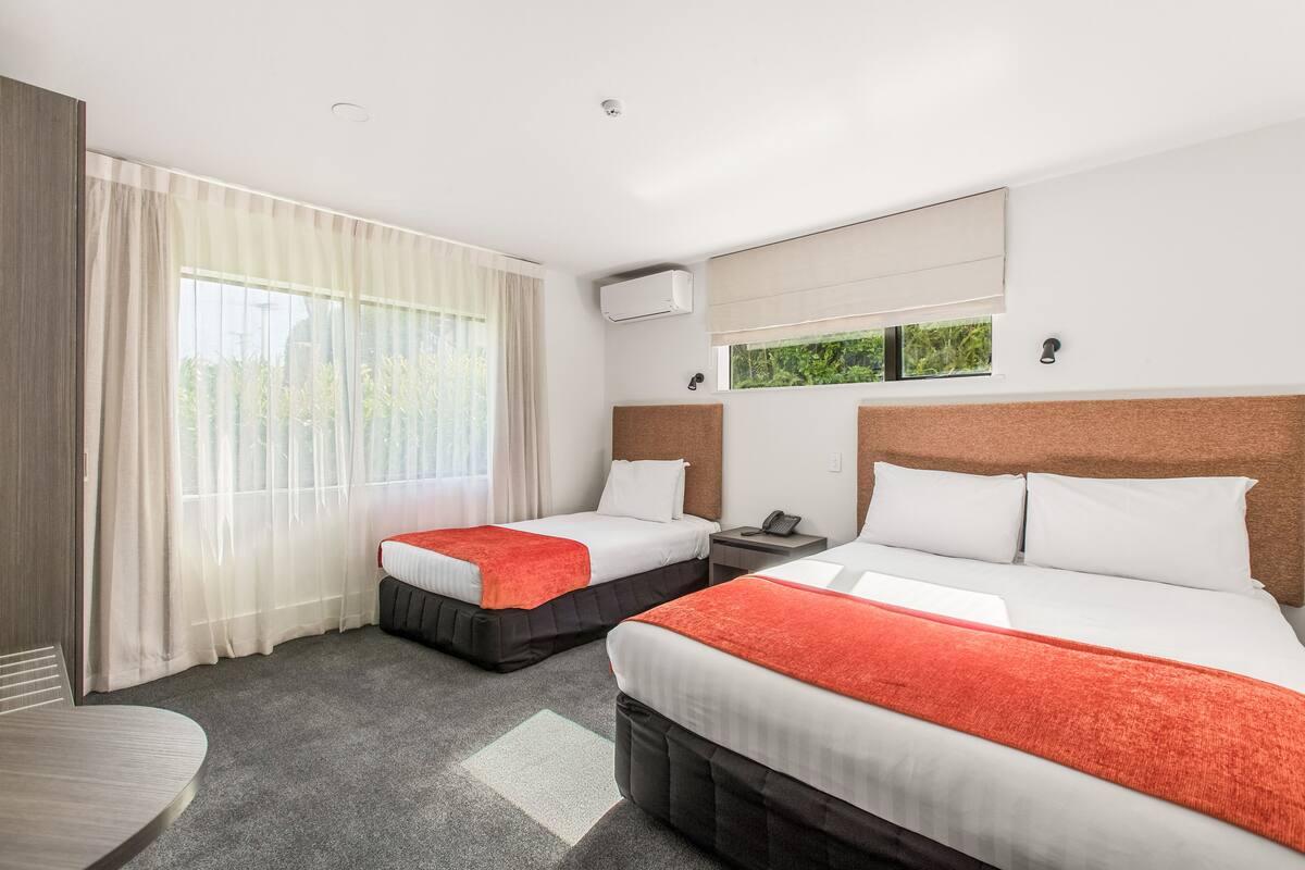 Quarto de hotel com duas camas, uma mesa e uma janela com cortinas.