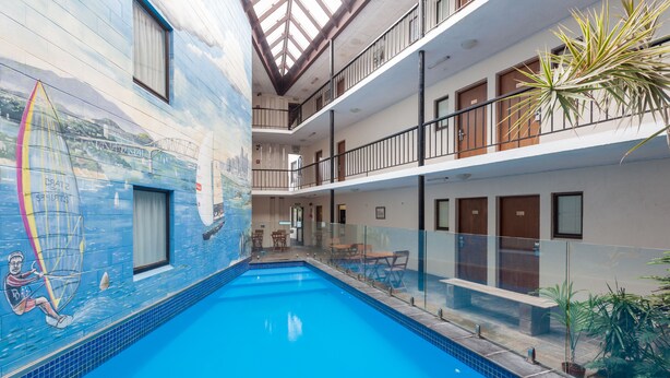 An indoor swimming pool with a mural of a surfer on the wall, a glass balustrade, and a multi-level balcony with doors. - The Surrey Hotel (Auckland)