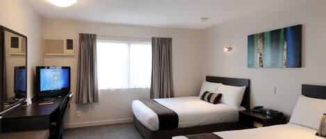 A hotel room with two beds, a desk with a computer, a window with curtains, and a painting on the wall.