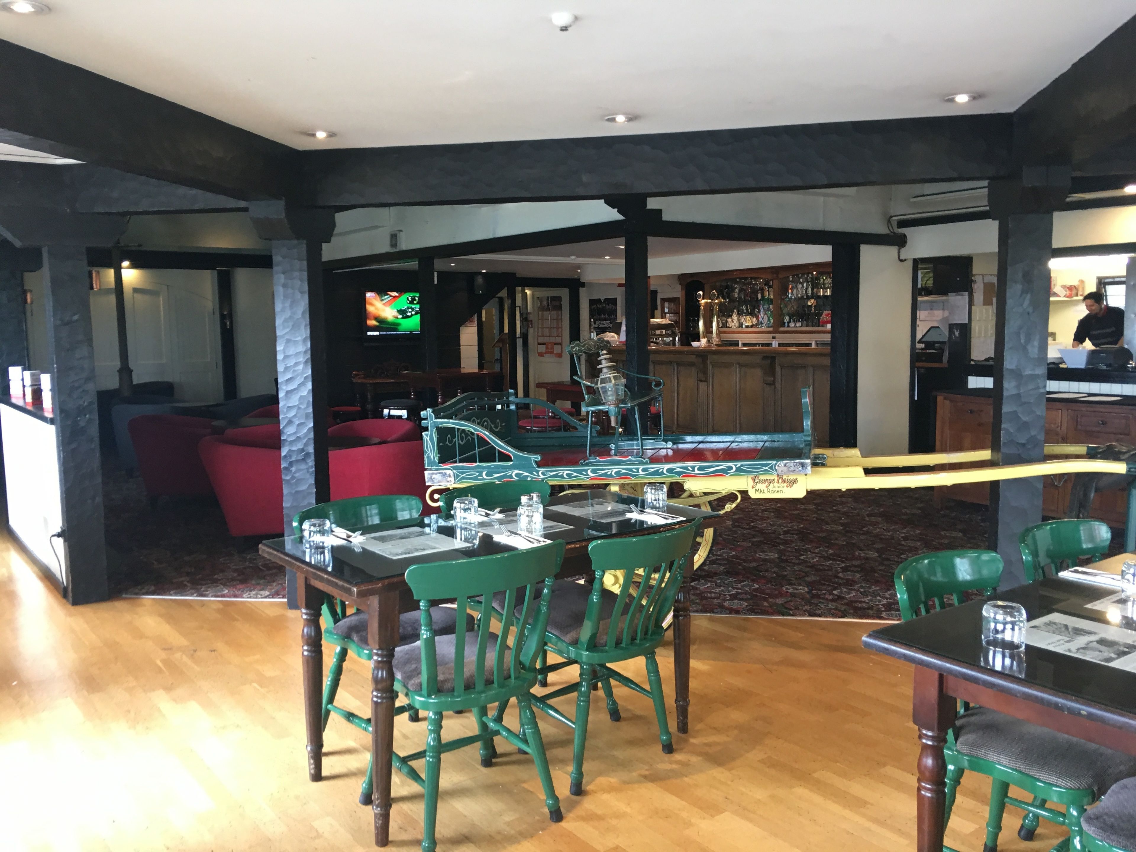 Ein Restaurant mit Holzboden, grünen Sitzmöglichkeiten und einer Bar mit Fernseher.