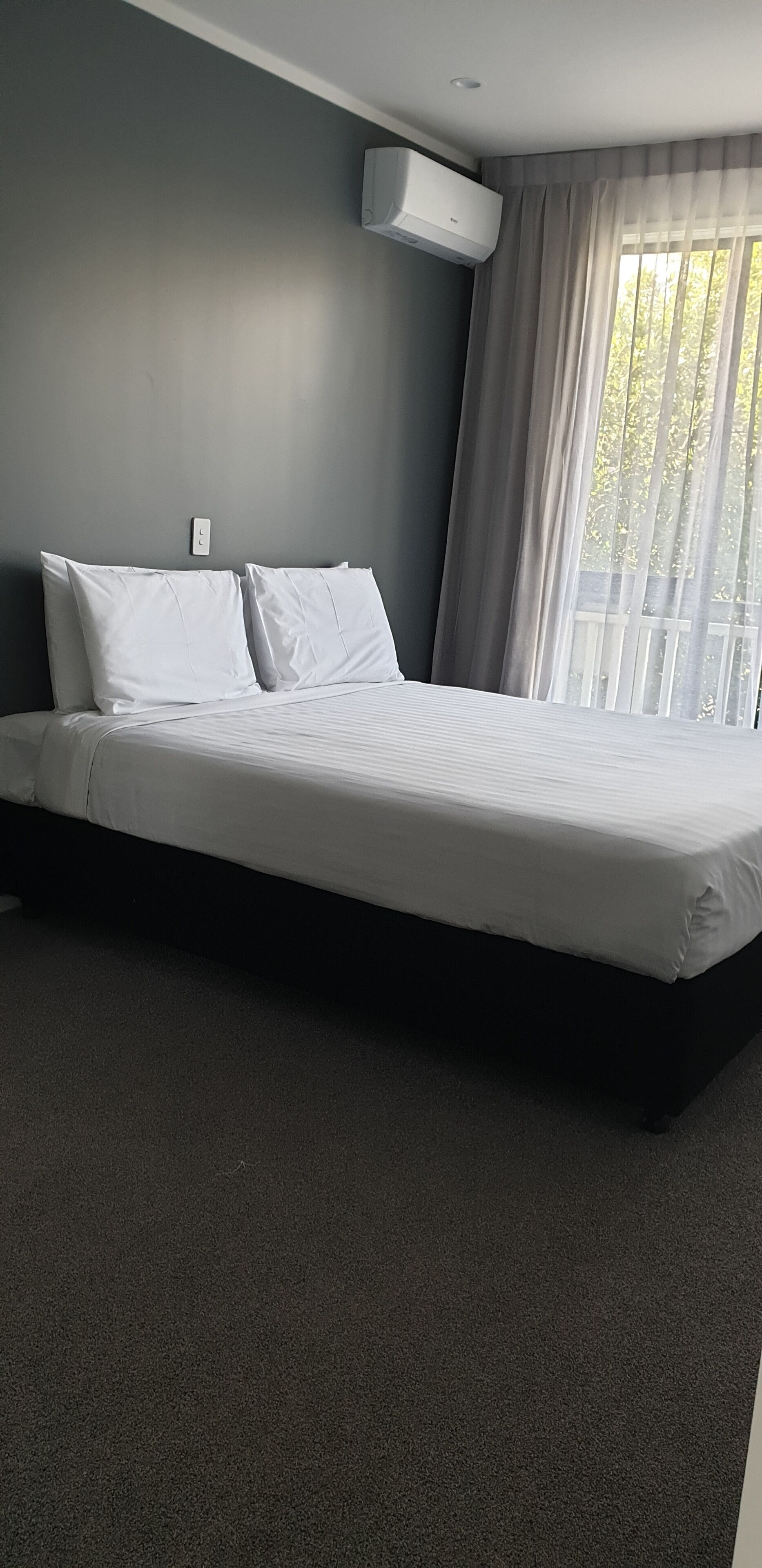 Et moderne hotelværelse med en stor seng, grå vægge og et vindue med lette gardiner.