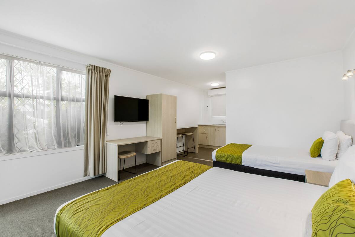 Quarto de hotel com cama, escrivaninha, televisão e banheiro.