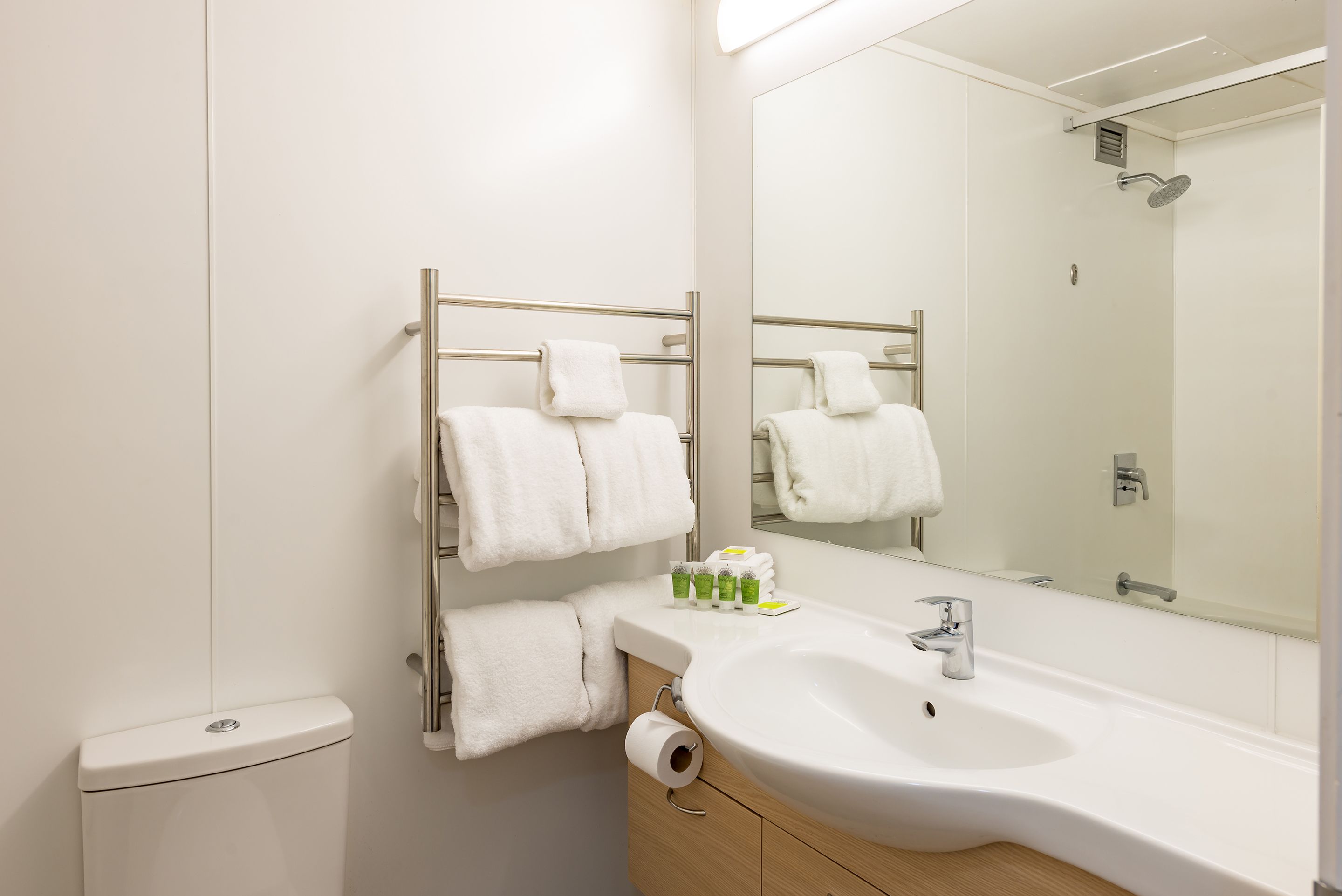 A modern bathroom with a white sink, a mirror, and a towel rack with multiple white towels.